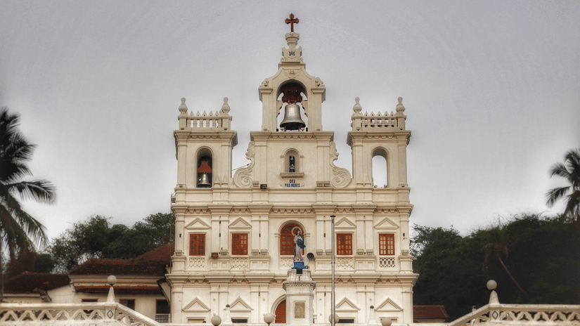 Front facade of a white colonial Portuguese church with twin towers and a cross in Goa.