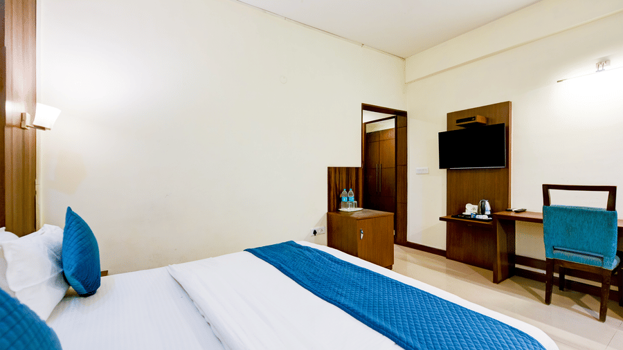 The Pamposh, New Delhi | A room with tables, a chair, a large bed, sporeads, pillows, and doors.