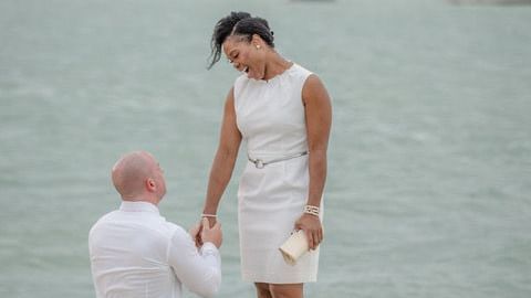 A person kneeling on the Casa Morada dock, holding the hand of his partner with calm waters in the background on a cloudy day.
