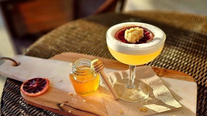 Glass of a pale beverage resting on a wooden serving board placed on a table.