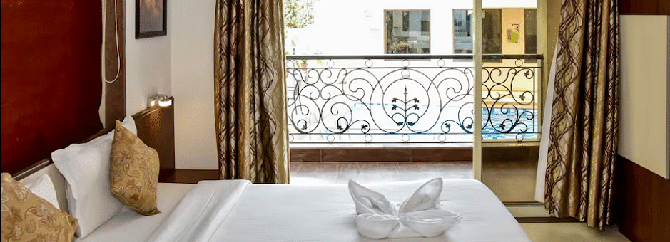 Cosy bedroom with golden cushions, towel swan decor, and a French balcony overlooking greenery at La Vida Studio Inn.