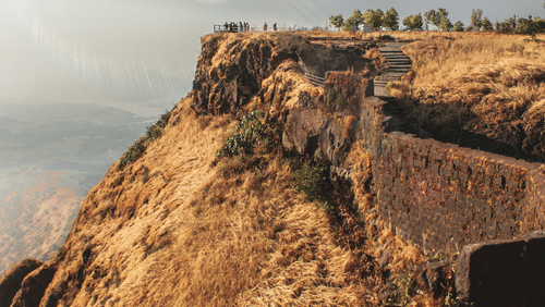 A rocky hillside with a fort, sparse vegetation, and a bright sky visible in the background.