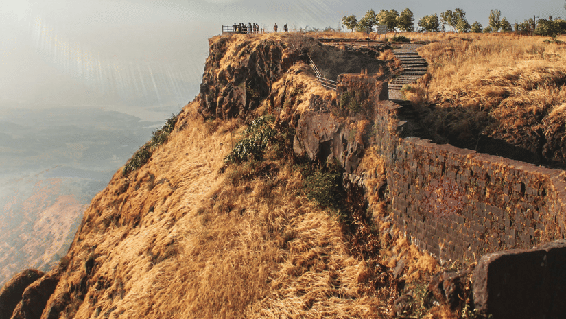 A rocky hillside with a fort, sparse vegetation, and a bright sky visible in the background.