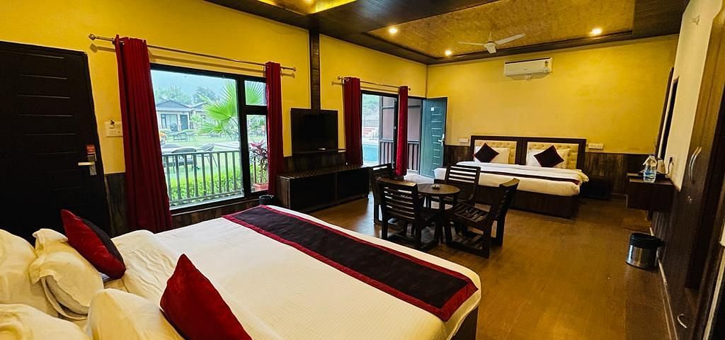 A Family Cottage with beds facing towards each other seperated by a round dining table and TV at DLS MJ River Resort, Rishikesh.