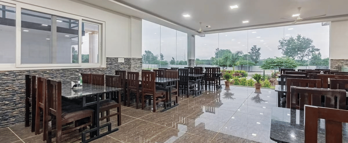 Well-lit restaurant with large windows offering scenic views and comfortable wooden seating at Siri Ambari Resorts and Spa.