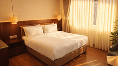 Bedroom of Pride Premier Darjeeling featuring a double size bed, bedside table with lamps on either side, and a large window with curtains drawn.