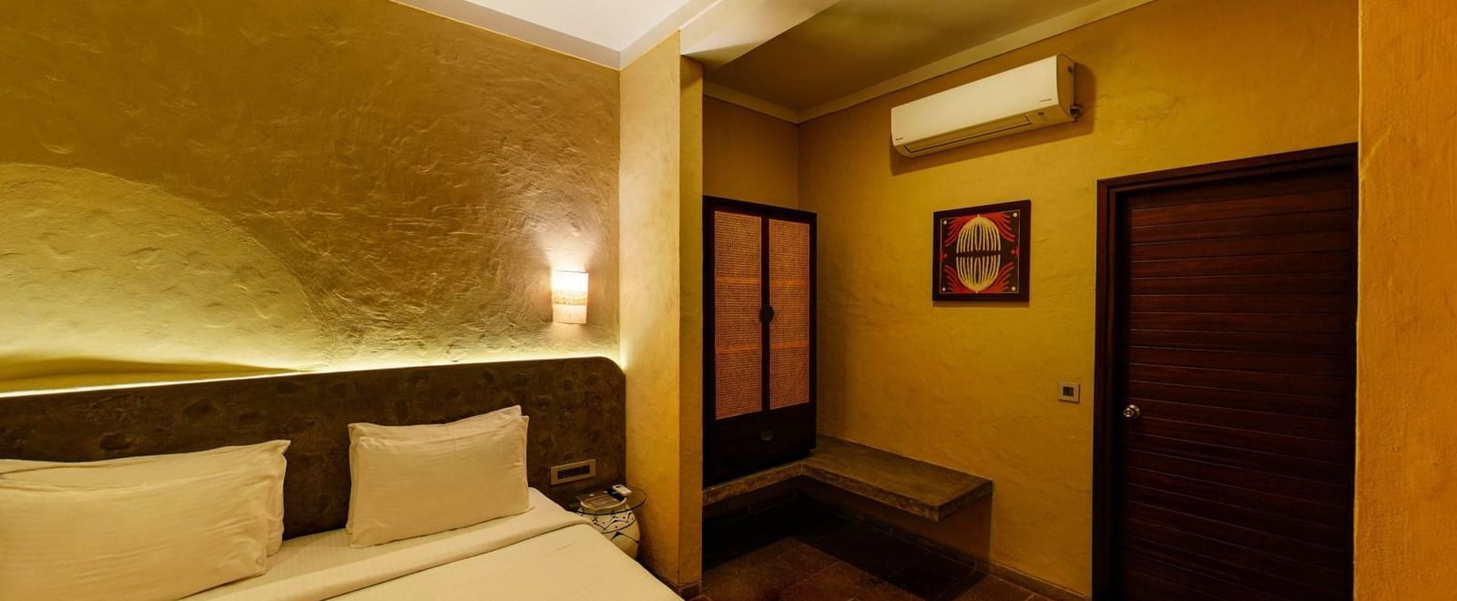 Room with partially visible bed, cushioned headboard, framed artwork on the wall, and wooden wardrobe at Fireflies Resorts, Kabini.