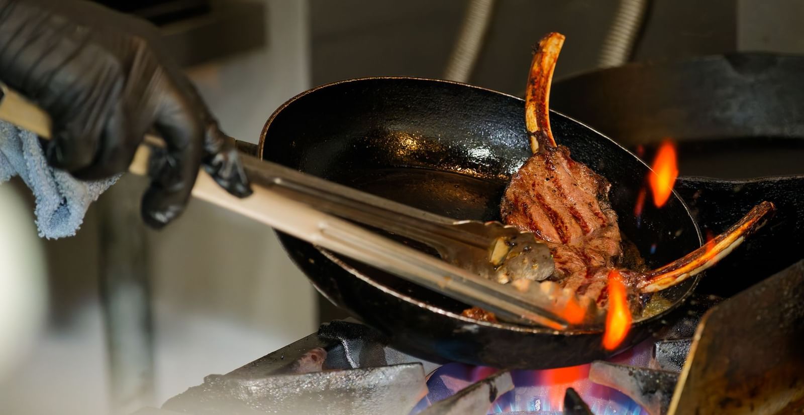 Chef at Narrow Gauge Inn grills bone-in meat over open flame in a hot skillet as part of a freshly prepared dish.