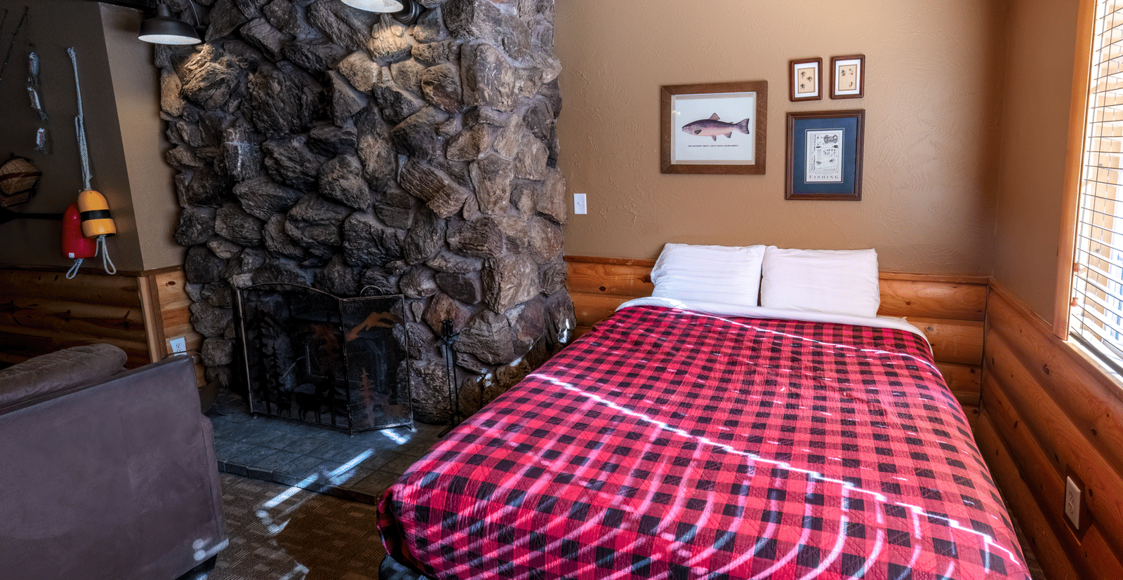 A cabin bedroom with a bed featuring a red and blue plaid comforter and a striking feature wall made of dark, rough-cut stone - Shaver Lake Village Hotel