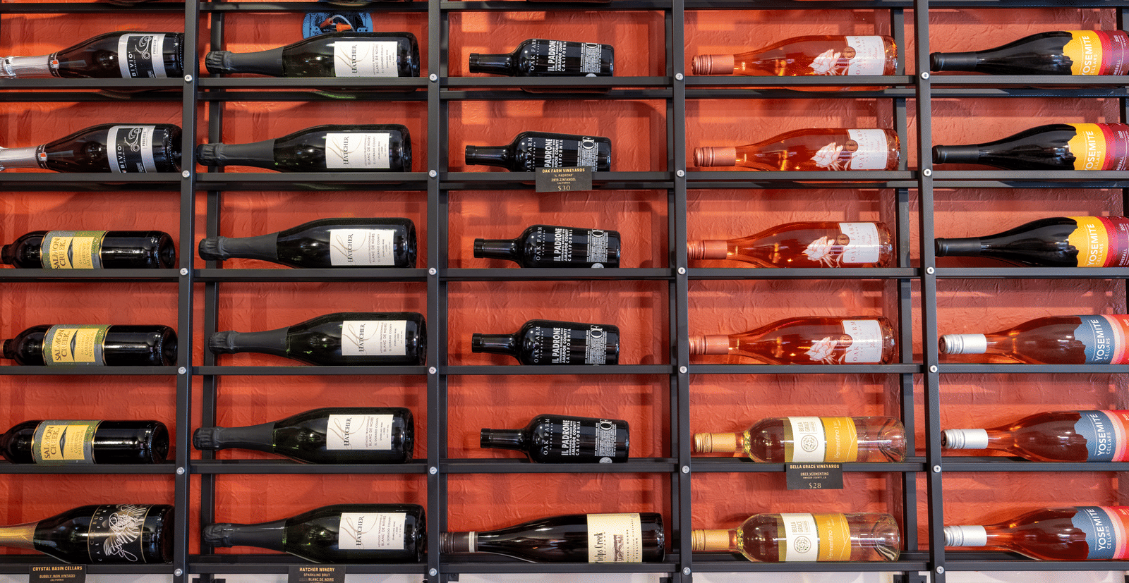  A wide shot of a large metal wine rack, displaying multiple rows of wine bottles on a red wall at Aroma Restaurant and Wine Bar at The Groveland Hotel.