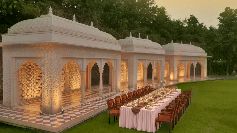 Elegantly set long dining table under ornate, domed structures on a green lawn at dusk at Heritage Village Resorts & Spa.