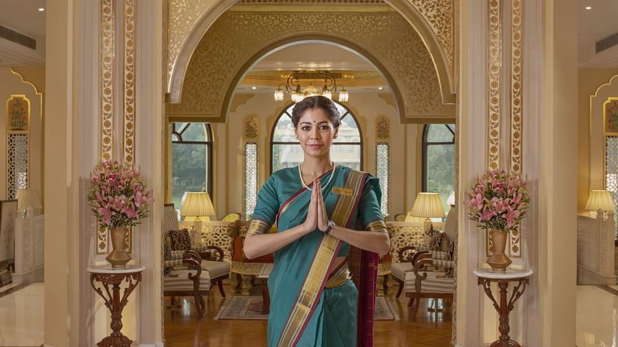 A woman dressed in a saree stands gracefully in the hotel lobby, posing with her hands joined in a traditional Namaste gesture - Heritage Village Resorts & Spa, Manesar