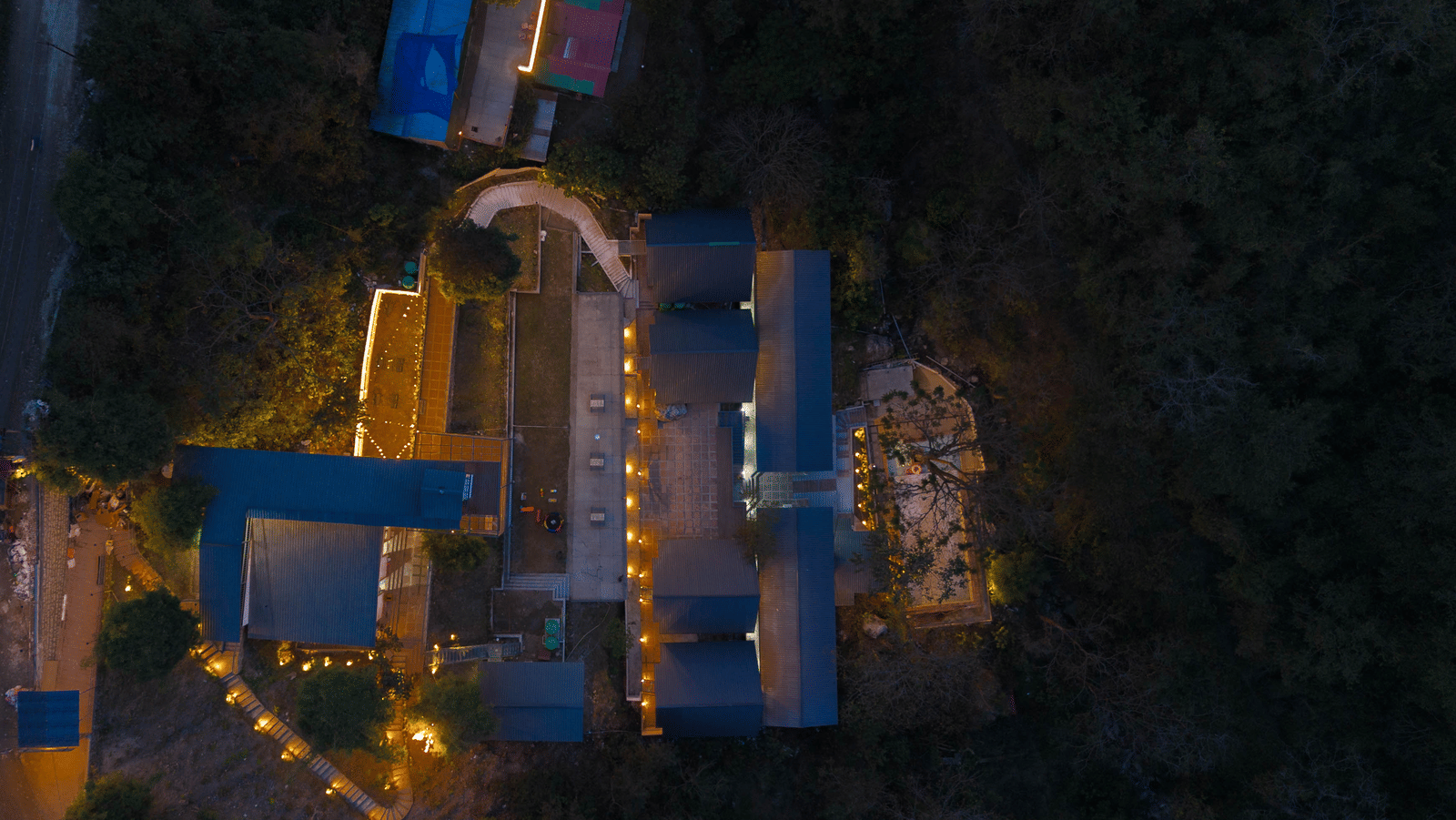 An aerial shot shows the resort buildings of Perfect Stayz The Jungle Resort illuminated at night.