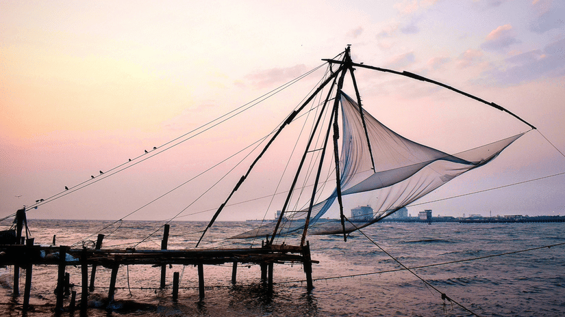 Chinese fishing nets standing along the Kochi waterfront beneath a soft pastel evening sky