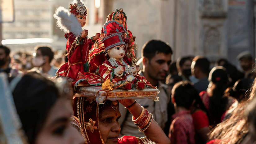 A woman in traditional Rajasthani attire carrying a decorated idol during the vibrant Gangaur festival procession.