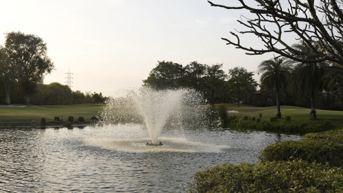 An overview of a fountain in a waterbody with greenery around - Karma Lakelands.