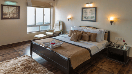 Polo Resort Cherrapunji bedroom with vaulted wood-beam ceiling, dark four-poster bed, recliner, framed art, window view and rug.