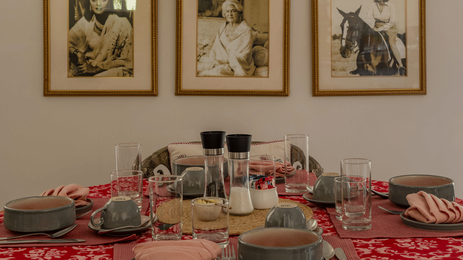 Dining area with a red-draped wooden table, tableware, and a gallery wall of framed photographs at Barwara Kothi, Jaipur.