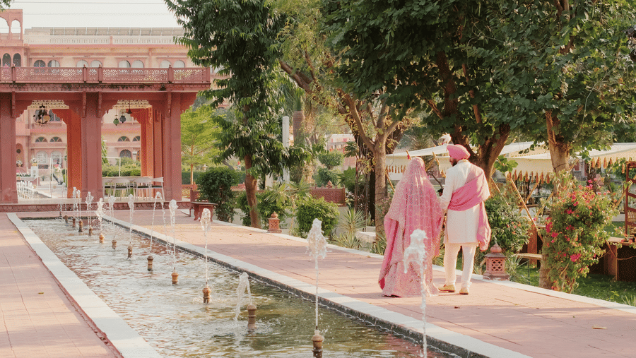 Bride Ritika and groom Jaswinder walking together beside long water garden at Umaid Palace wedding