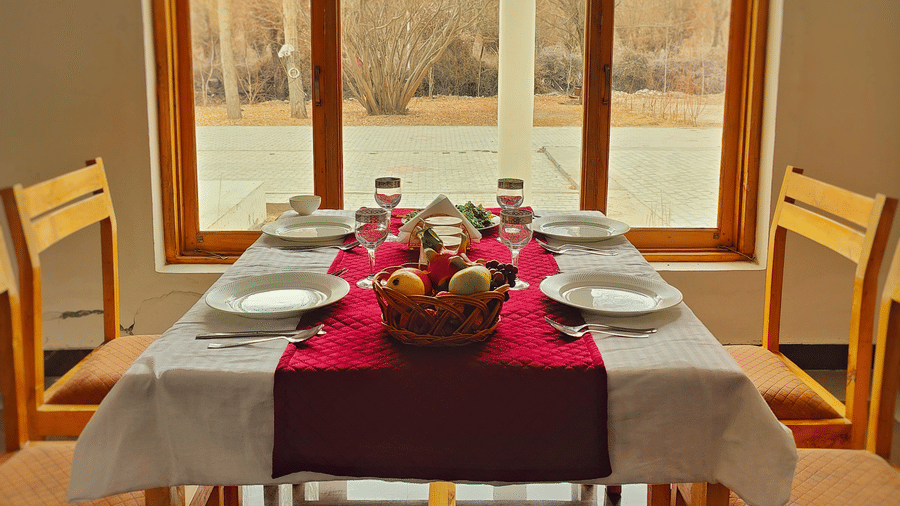 A wooden dining table for four set neatly in front of a large window with a scenic view at Indus Serenity Retreat.