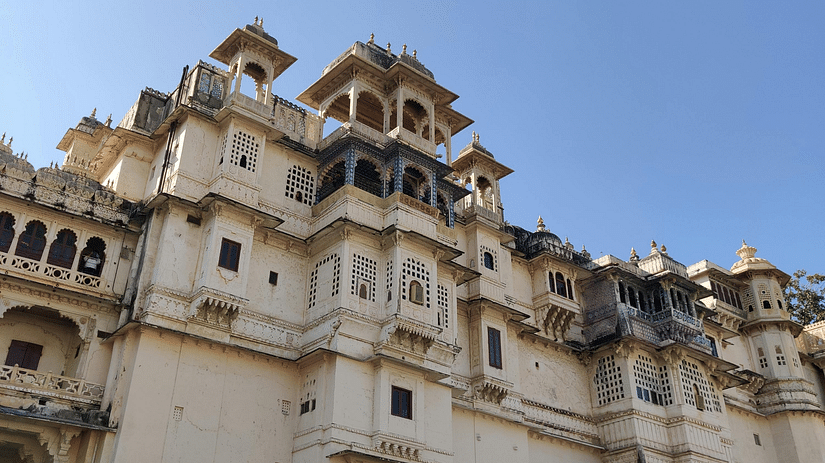 Low-angle shot of a palace, featuring its facade with multiple levels, balconies, and decorative elements under a clear blue sky.