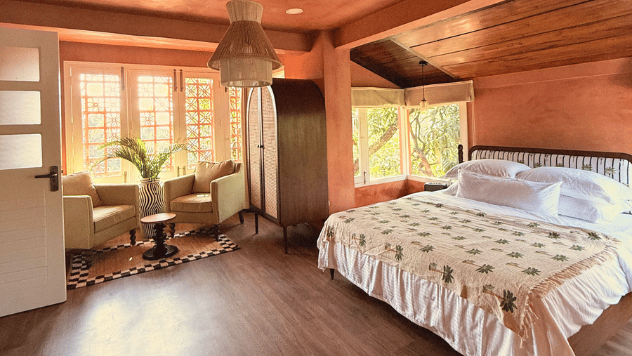 Penthouse Suite at The Unseen Boutique Hotel featuring a plsuh bed by a window and a seating space near it with sunlight coming through the window