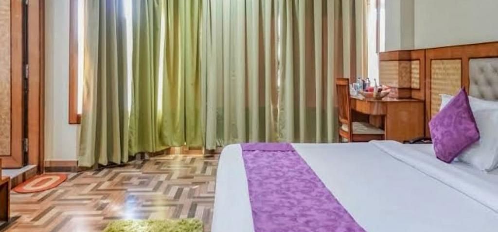 A spacious bedroom with rich wooden flooring, green drapes, and a purple-accented bed for a cosy stay - Pemaling Lords Eco Inn Guwahati