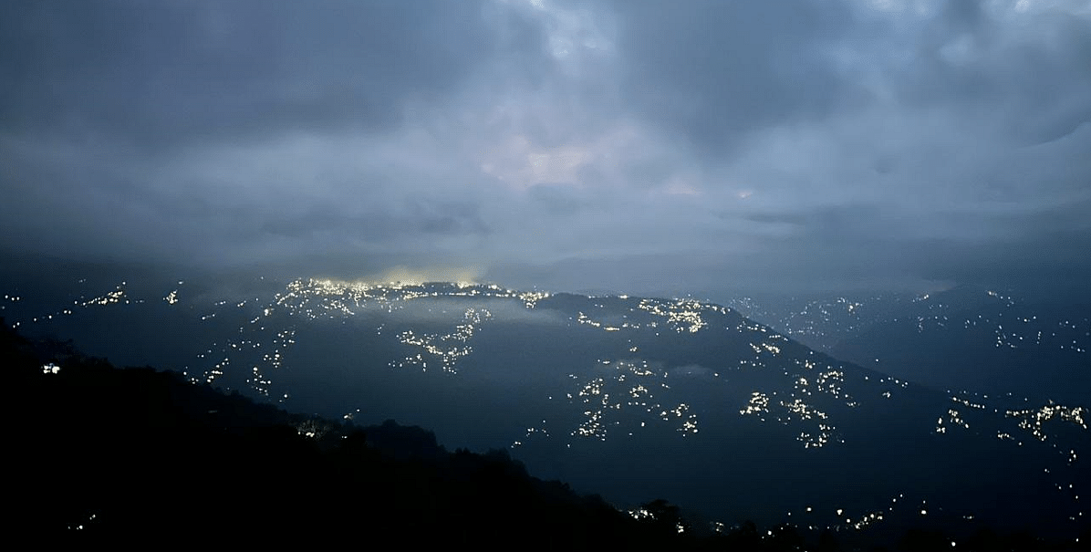 A panoramic view of a city or town at night from a high vantage point, with scattered lights, possibly visible from Summit Enigma Resort and Spa.
