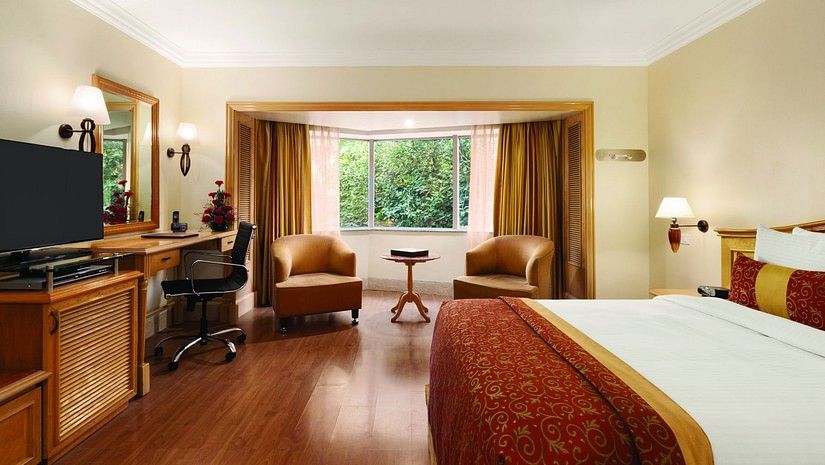 An image of a Deluxe Room featuring bed, flat screen TV, lamps, work desk, chair, sofa set and table - Ramada Plaza by Wyndham Palm Grove