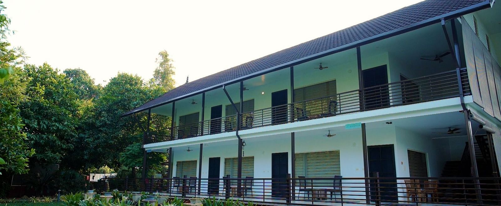 A two-story building with a white facade and dark accents is situated amidst lush greenery, with a well-maintained lawn in the foreground.