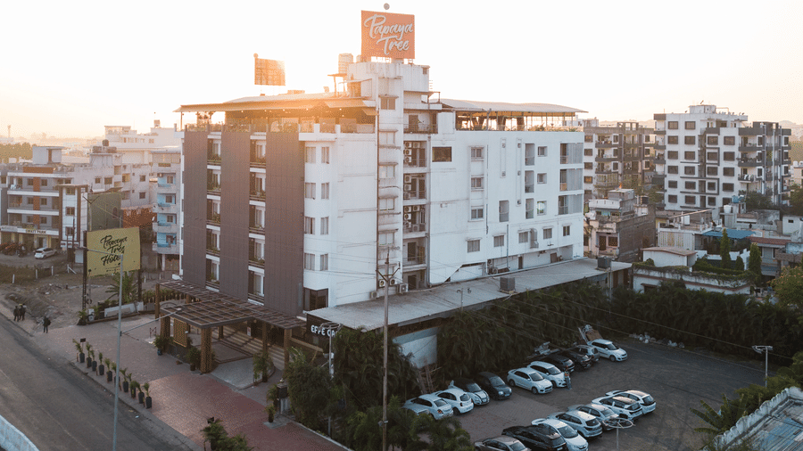 A wide exterior view of Papaya Tree Hotels captured during sunset, highlighting the building’s white facade, rooftop area, and surrounding city streets with parked vehicles.
