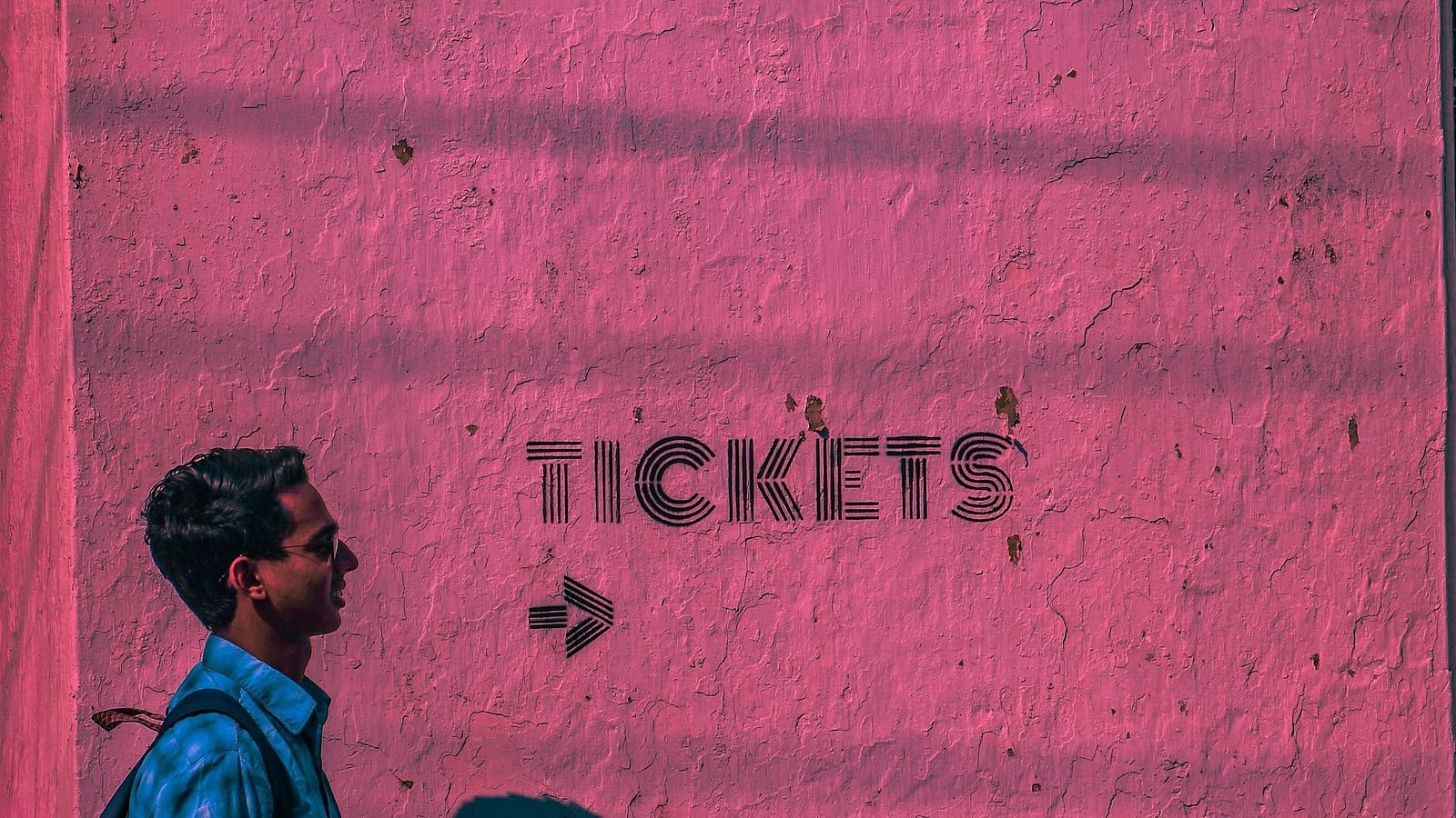 An image where the text on a pink wall says- tickets and showing an arrow towards right and a man going in that direction.