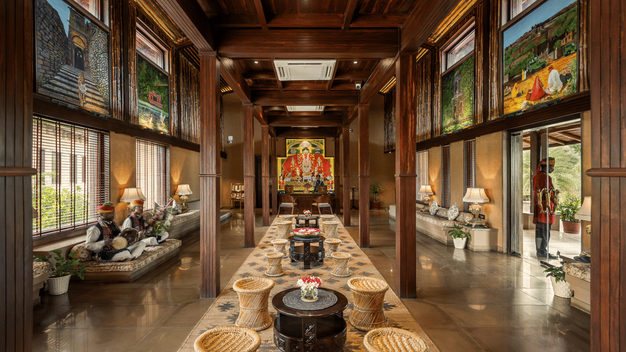 Grand timber-framed reception hall at AamaGhati Wildlife Resort featuring traditional Rajasthani artwork, central woven stool seating, and live folk musicians seated near the entrance.