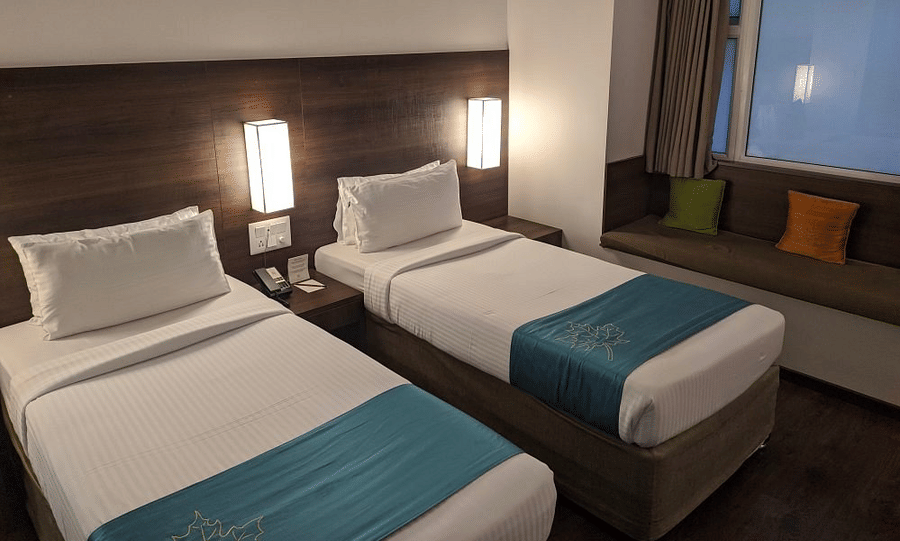 The Comfort Room at Temple Tree Hotel, Bangalore showcasing twin beds, a wooden head board, overhead lamps, and a large glass window.