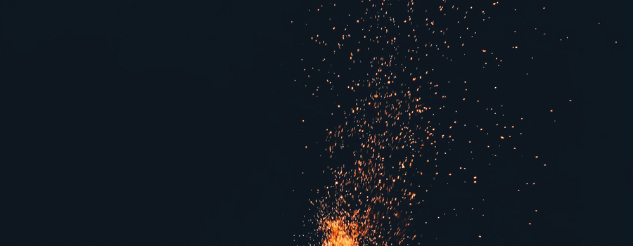 A bright bonfire burning in the darkness with sparks rising into the night air.