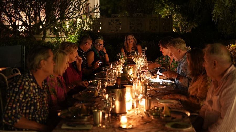 A group of guests enjoy an intimate candlelit dinner outdoors, surrounded by nature at night - Khas Bagh, Jaipur.