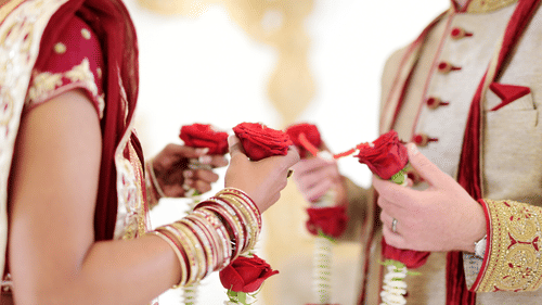 A close-up of a bride and groom's hands, with the bride's hand decorated with henna, holding red roses together.