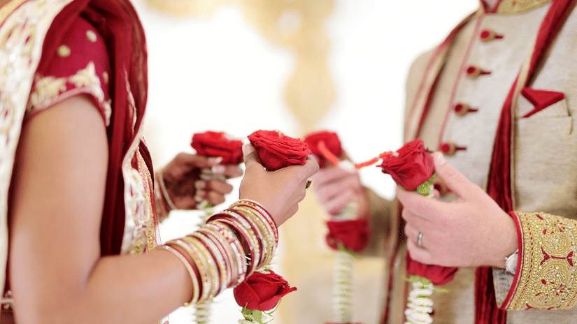 A close-up of a bride and groom's hands, with the bride's hand decorated with henna, holding red roses together.