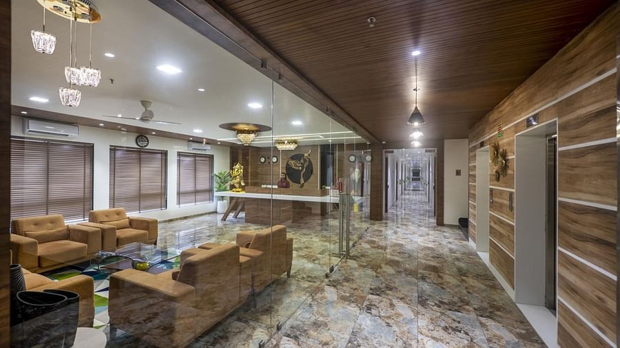 A lobby with armchairs and sofas arranged for seating, and a patterned floor leading to a reception area  at Angel Lords Eco Inn Amreli.