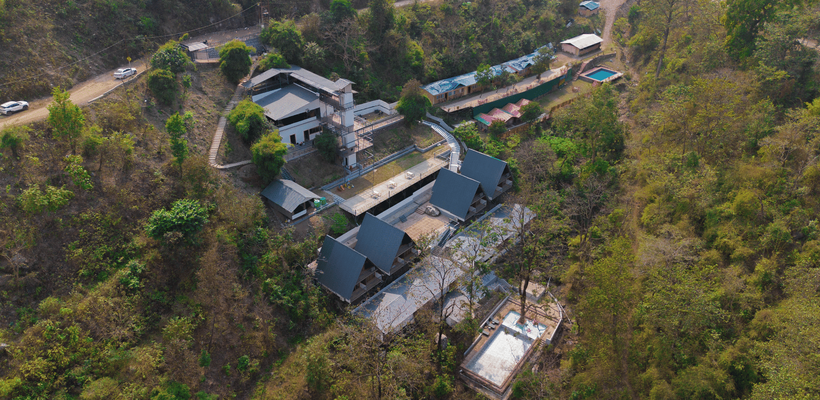 An aerial shot shows the resort buildings of Perfect Stayz The Jungle Resort surrounded by trees and hills.