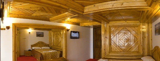 Hotel room with a bed featuring elaborate wooden carving, a red carpet, and a wooden ceiling at Hotel Dolphin Darjeeling.