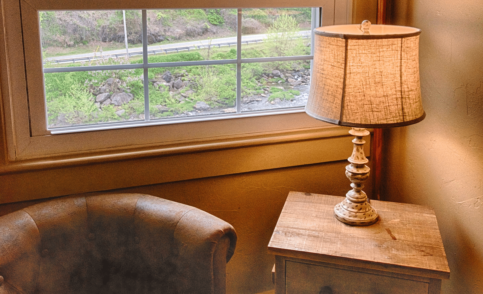 a close up image of a leather arm chair kept alongside a wooden table with a lamp over it - Historic Tapoco Lodge