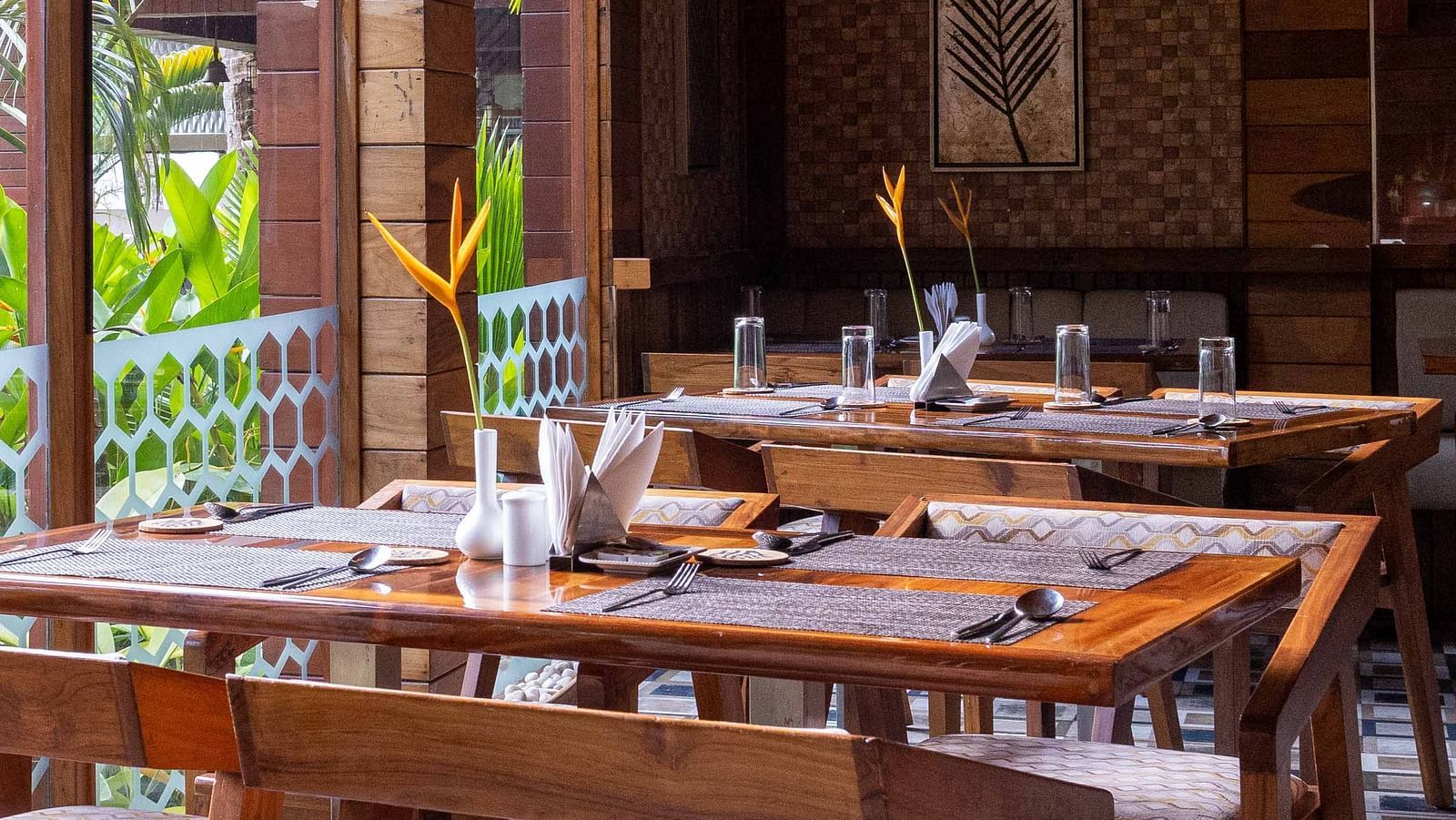 A spacious dining area at Ocean Prime with wooden tables and chairs, set in a modern wooden room. The decor is minimalist, with large windows offering a glimpse of the outside greenery - Coral Reef Resort & Spa, Havelock