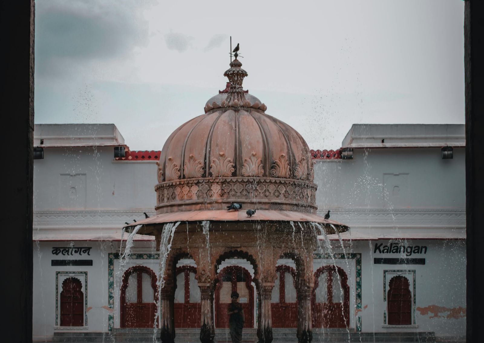 A brown concrete fountain in front of a white building, of Saheliyon ki Bari.