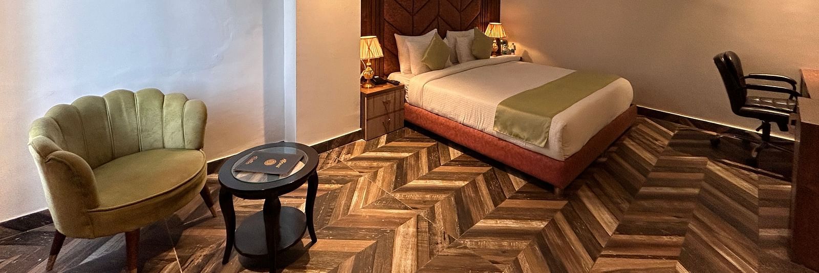 Image of Super Deluxe Room at DLS Grand Luxotica, Dehradun featuring a sitting space including a couch and a coffee table placed at a distance from the plush bed under warm lighting