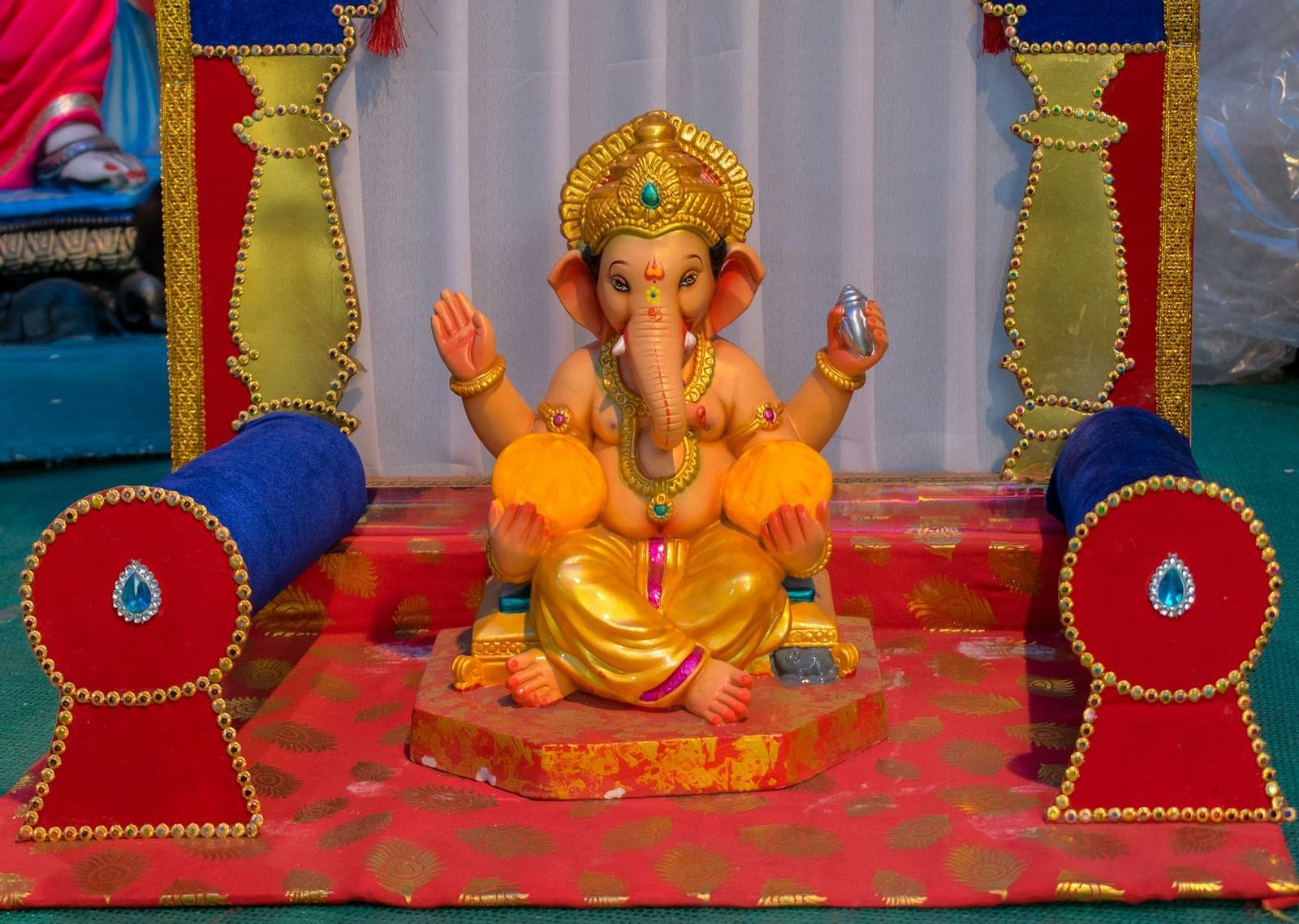 An overview of a ganesha's idol kept on a small pedestal with pillows next to it.