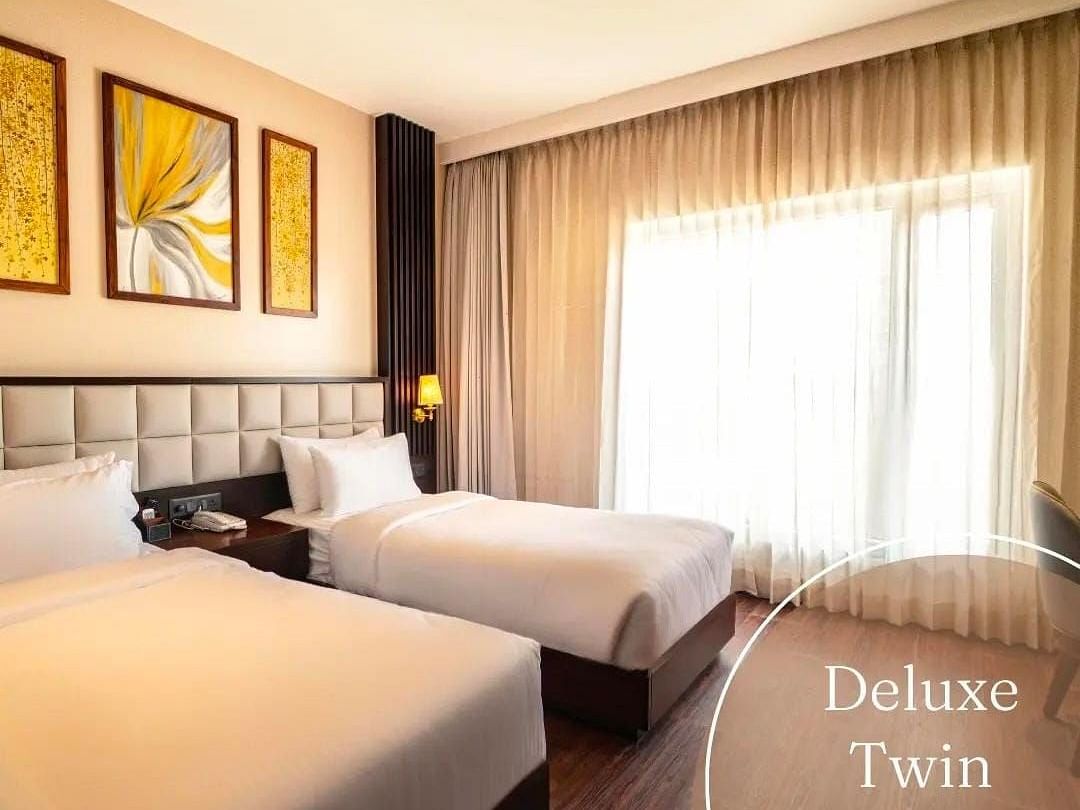 A image of a room with twin beds and lights seeping into the room from a window