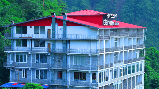 Facade of SPT Clarks Inn Suites, Mandi amidst lush greenery with a glimpse of a mountain in the bakcground