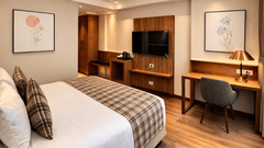 Bedroom at Pride Premier Darjeeling featuring a bed, a flat TV screen mounted on the wall, work desk and chair, and tea and coffee maker.