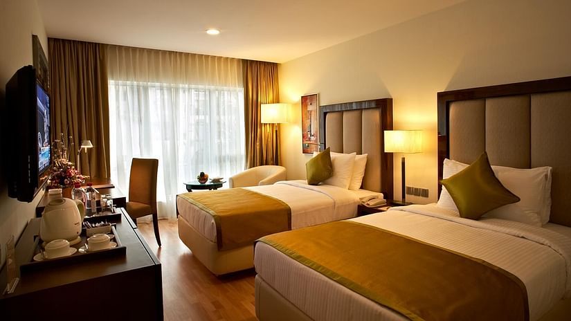 An image of a bedroom featuring twin bed, bedside table with lamps, flat TV screen, a cabinet with tea and coffee maker and a work desk and chair at Adarsh Hamilton